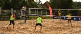 Mistrzostwa Polski Strażaków Państwowej Straży Pożarnej w Siatkówce Plażowej. Zdjęcie przedstawia strażaków PSP podczas meczu na boisku plażowej piłki siatkowej. 