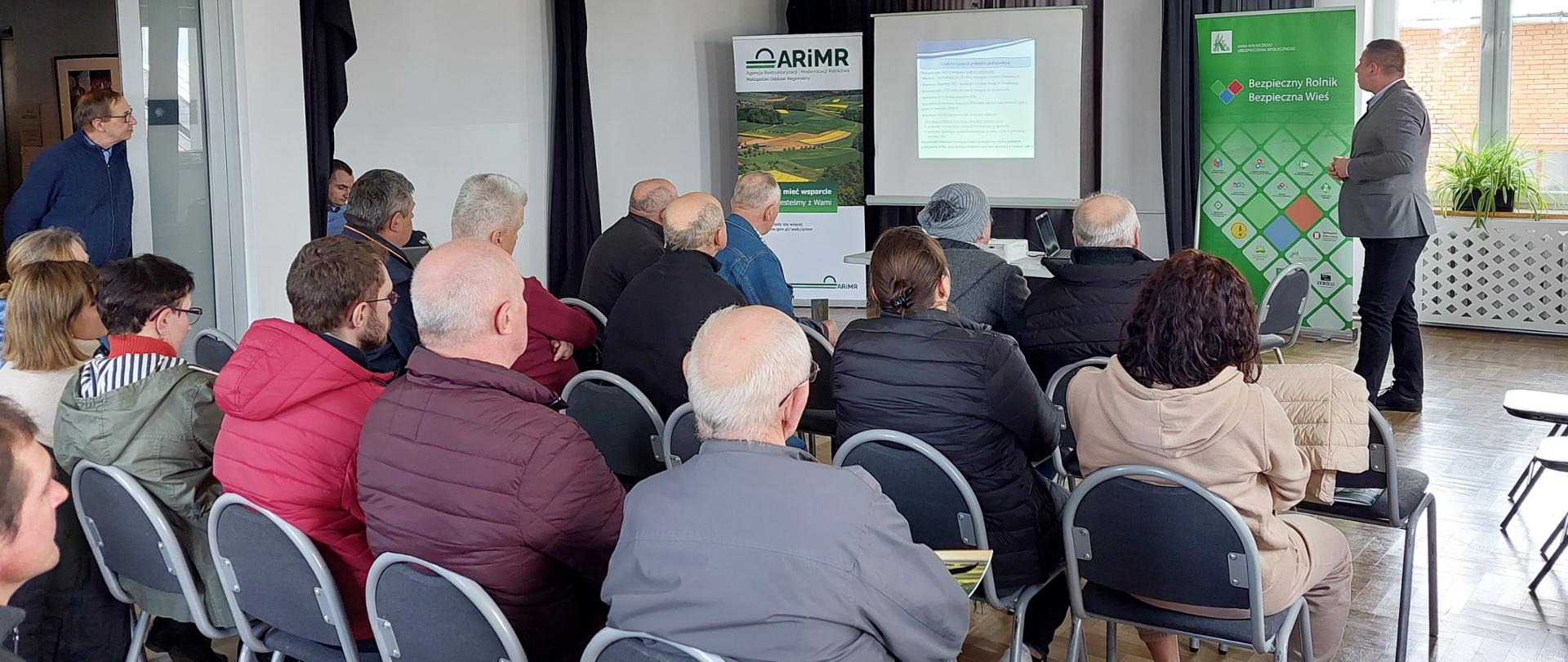 Widok sali szkoleniowej i grupy uczestników, na drugim planie mężczyzna omawiający prezentację