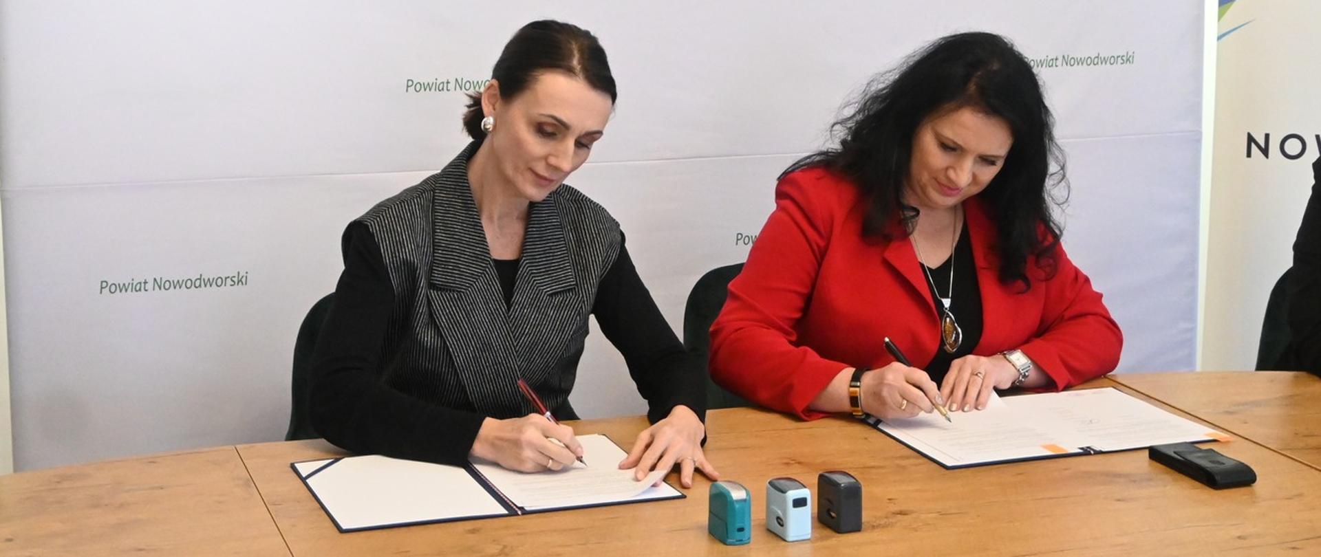 dwie kobiety siedzą przy biurku i podpisują umowę