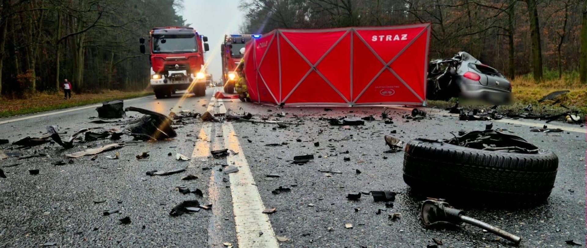 rozbite auto po wypadku oraz rozrzucone elemnty na drodze. W tle ppojazdy strażackie