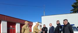 Zdjęcie przedstawia moment przekazania samochodu operacyjnego z Komendy Powiatowej PSP w Lubinie do OSP Chobienia. Przekazanie odbywa się na placu wewnętrznym Komendy Powiatowej PSP w Lubinie.