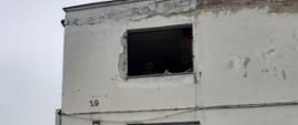 Fotografia przedstawia budynek koloru białego z uszkodzoną futryną okienną w wyniku wybuchu gazu. 