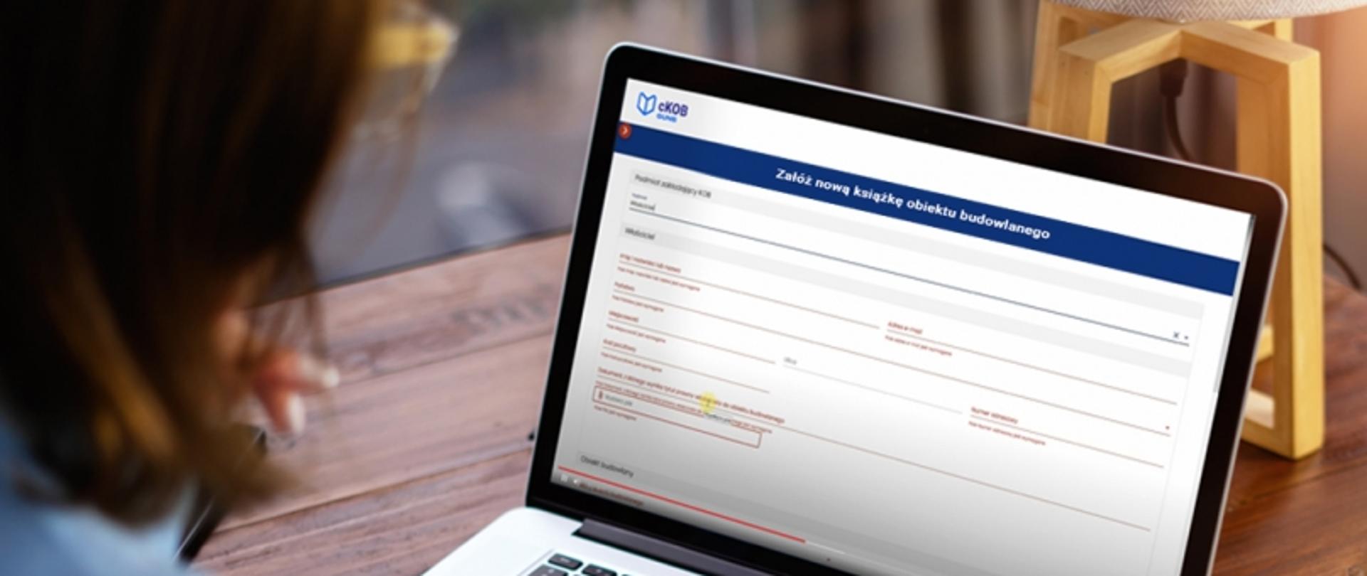 Osoba korzystająca z laptopa, na ekranie formularz do założenia książki obiektu budowlanego z polami takimi jak nazwa i adres obiektu.