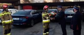 Na zdjęciu Komendant Powiatowy w mundurze galowym wręczający kwiaty strażakowi, który odchodzi na emeryturę.