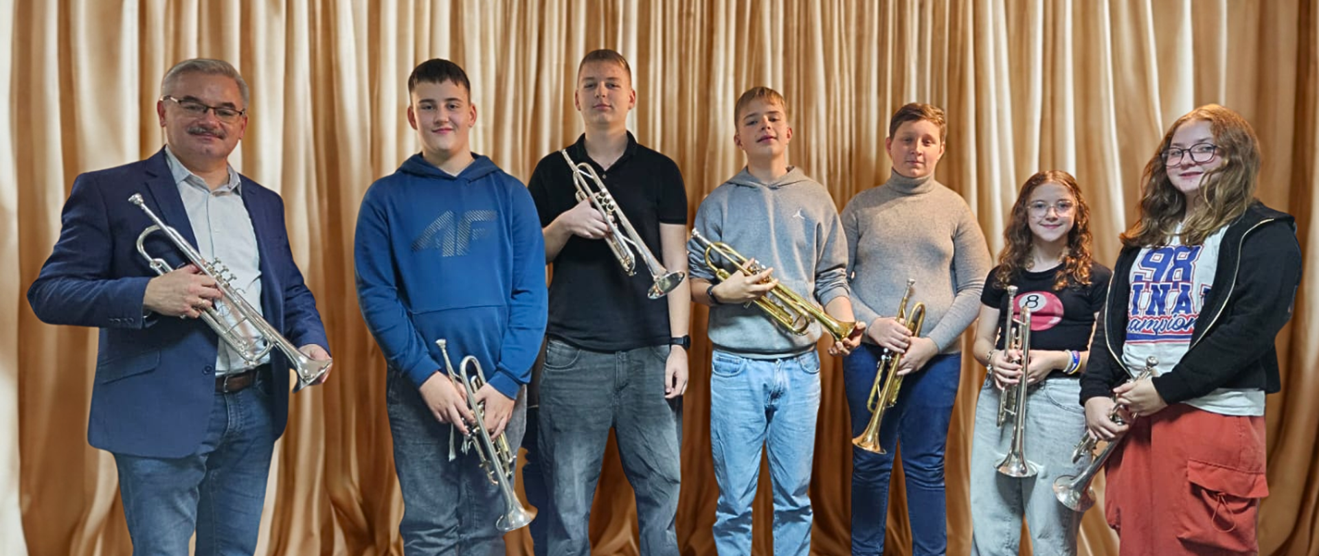 grupa kilku osób trzymających trąbki na tle beżowej zasłony