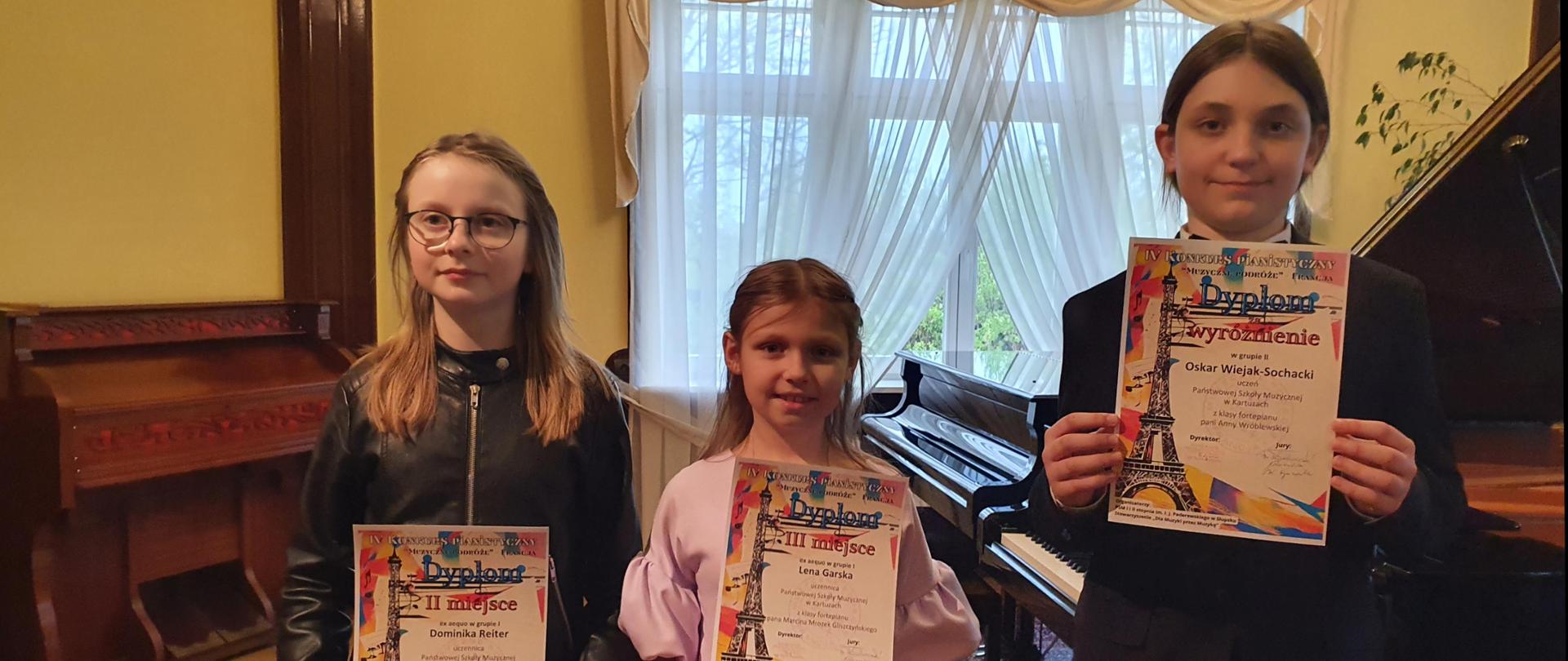 Uczniowie trzymający w dłoniach dyplomy, w tle fortepiany i pianino