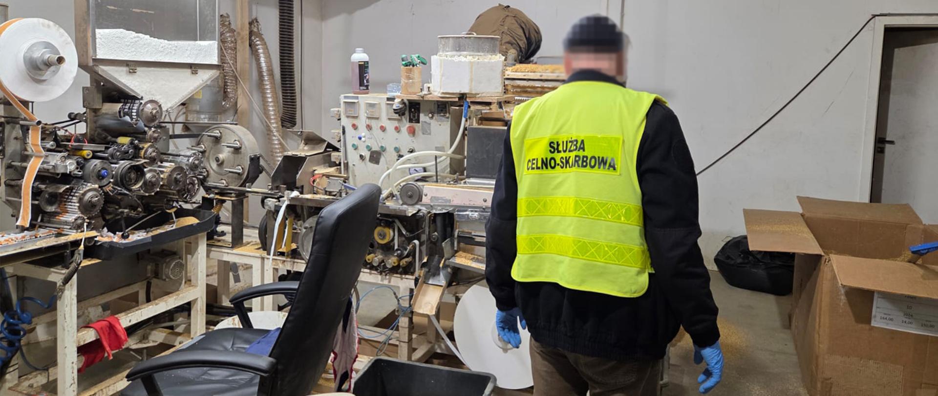 Pomieszczenie z maszynami produkującymi papierosy, obok niej osoba w kamizelce Służby Celno-Skarbowej 