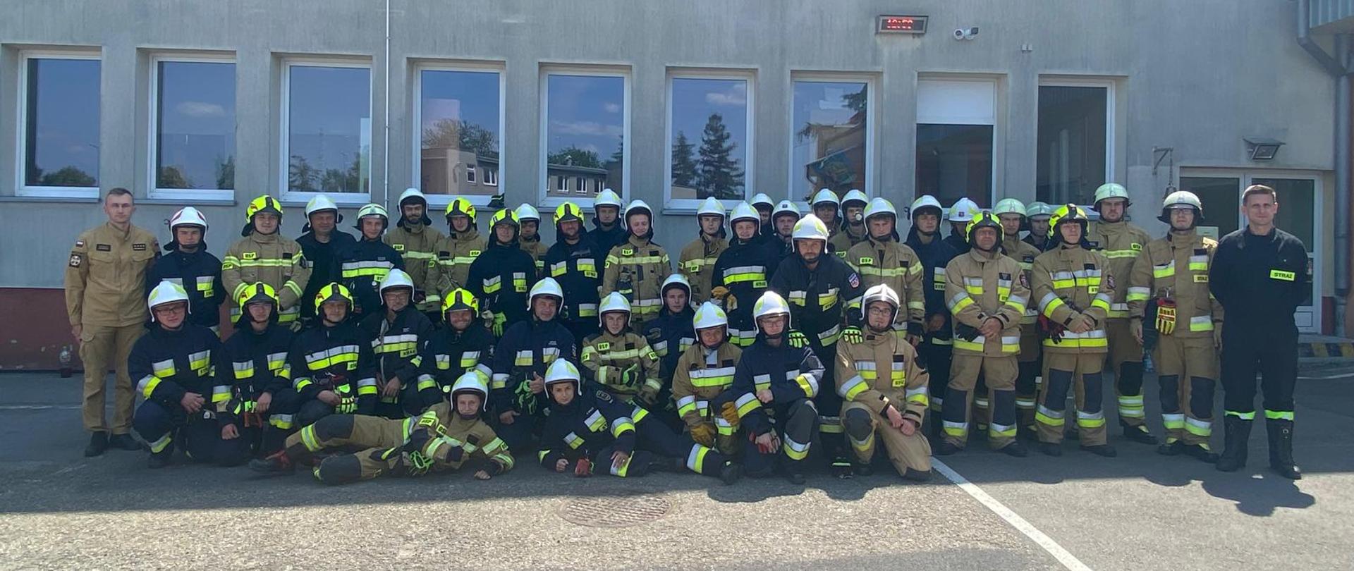 grupa strażaków – słuchaczy kursu, w tle budynek Komendy
