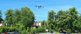 Dwie osoby stoją na trawiastym polu z rzędami roślin, nad nimi leci dron