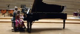 Dziewczynka i kobieta grają na fortepianie na 4 ręce.