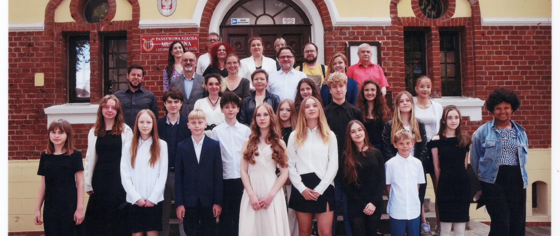 Zdjęcie absolwentów rocznika 2025 wraz z nauczycielami na schodach wejściowych do szkoły