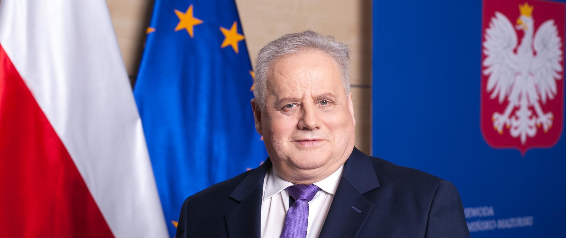 mężczyzna w ciemnym garniturze na tle flag 