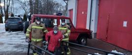 Zdjęcie przedstawia samochód strażacki na tle wejścia do budynku Niepublicznego Zakładu Opieki Zdrowotnej w Skotnikach. Na zdjęciu widać dwóch strażaków pomagających osobie starszej wejść do ośrodka zdrowia