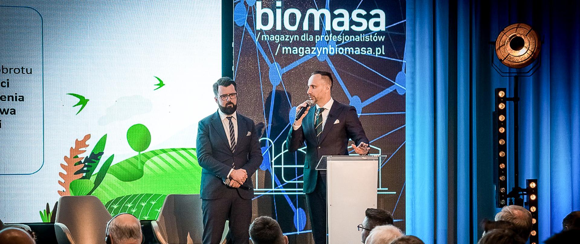 sekretarz stanu Janusz Kowalski stojący przy mównicy z mikrofonem w dłoni
