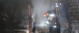 Pożar połaci dach budynku gospodarczego o wielkości piętnastu metrów kwadratowych. Centralnie widać strażaka podczas dogaszania konstrukcji dachu. 