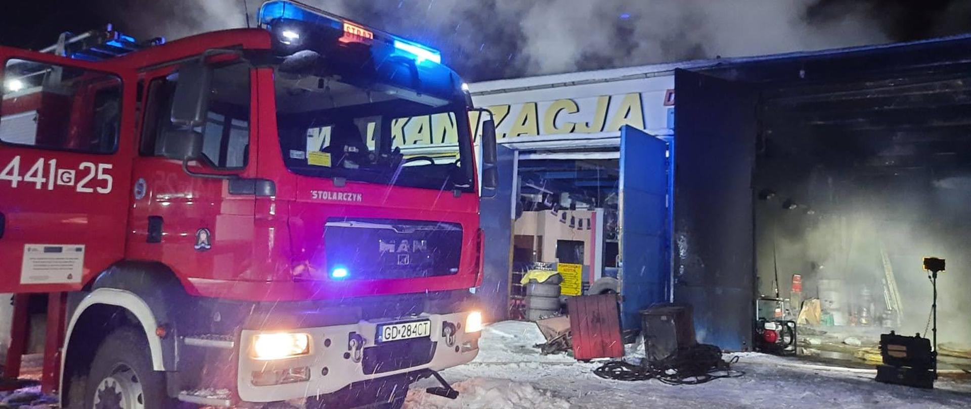 Samochód strażacki na tle budynku objętego pożarem