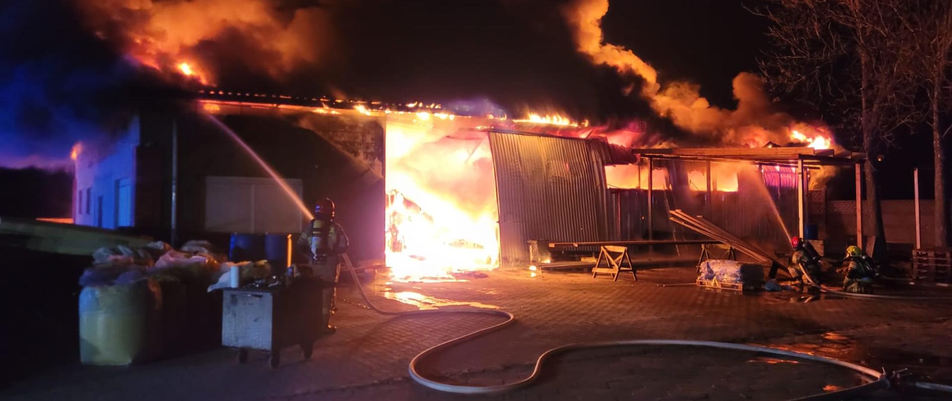 Strażacy podają dwa prądy gaśnicze na objęty pożarem budynek gospodarczy