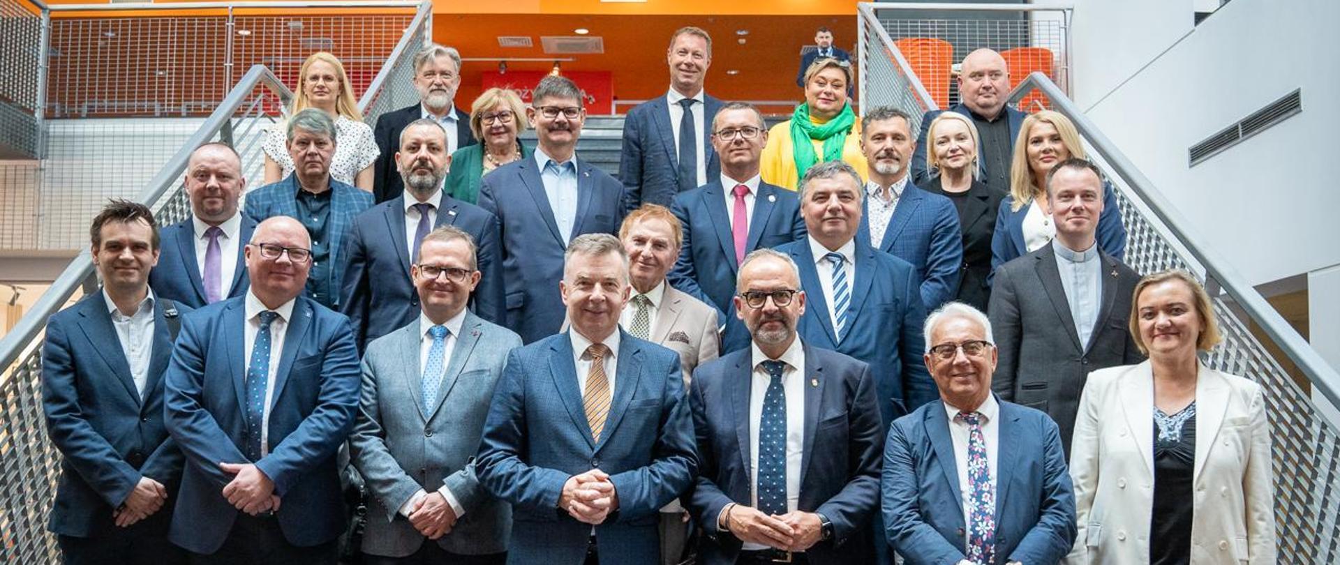 Zdjęcie zbiorowe, na metalowych schodach stoi duża grupa ludzi, pośrodku grupy minister Wieczorek.