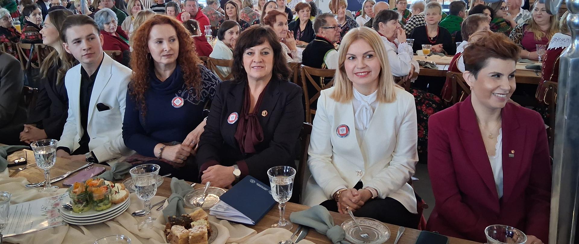 W przestronnej, elegancko udekorowanej sali liczna grupa uczestników siedzi przy stołach ustawionych w rzędach. Na pierwszym planie widać osoby w odświętnych strojach: Panią Izabelę Katarzynę Szamrej zastępcę Podlaskiego Państwowego Wojewódzkiego Inspektora Sanitarnego, Panią Ewelinę Stefanię Chojnowską Kierownika Oddziału Bezpieczeństwa Żywności i Żywienia Wojewódzkiej Stacji Sanitarno-Epidemiologicznej w Białymstoku oraz Panią Agnieszkę Sawczyńską z Oddziału Bezpieczeństwa Żywności i Żywienia Wojewódzkiej Stacji Sanitarno-Epidemiologicznej w Białymstoku