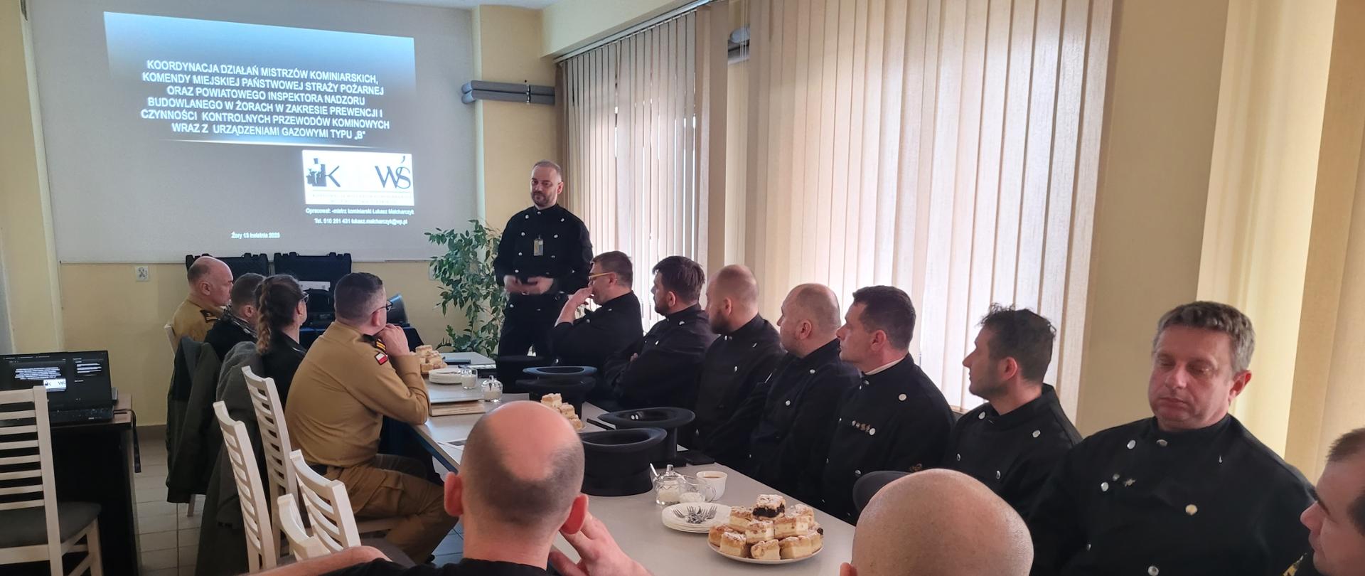 Osoby siedzą przy stole konferencyjnym. w Tle ścianka firmowa Państwowej Straż Pożarnej. 