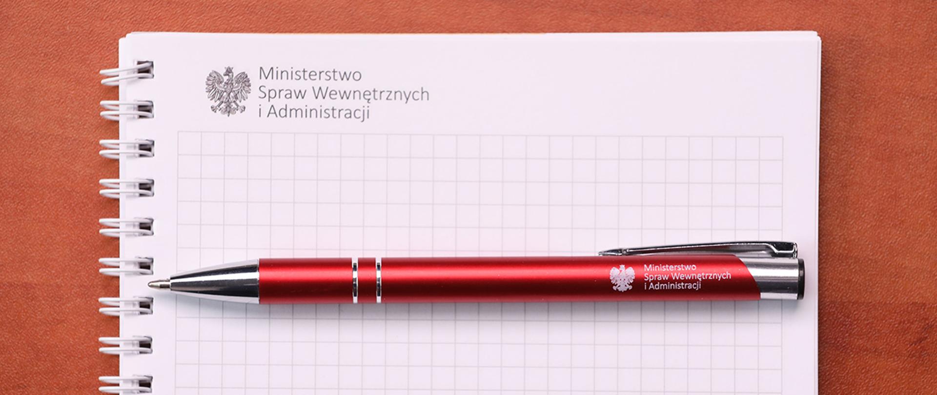 Otwarty notes MSWiA, na nim długopis z logo resortu