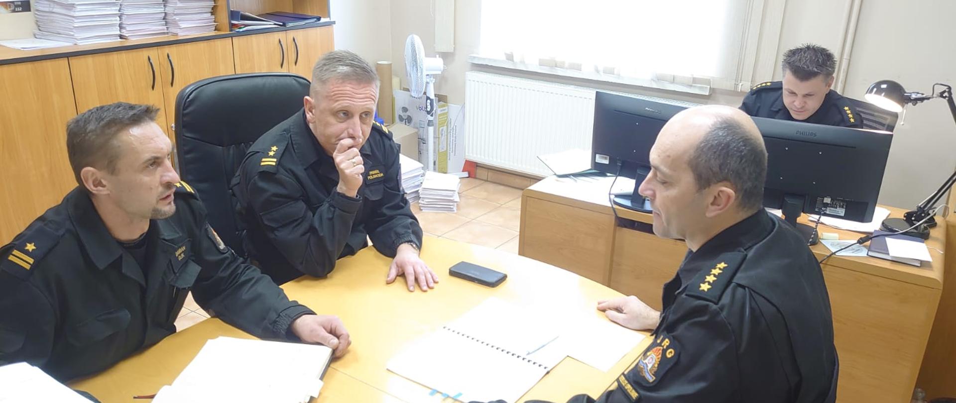 Zdjęcie przedstawia czterech strażaków w biurze