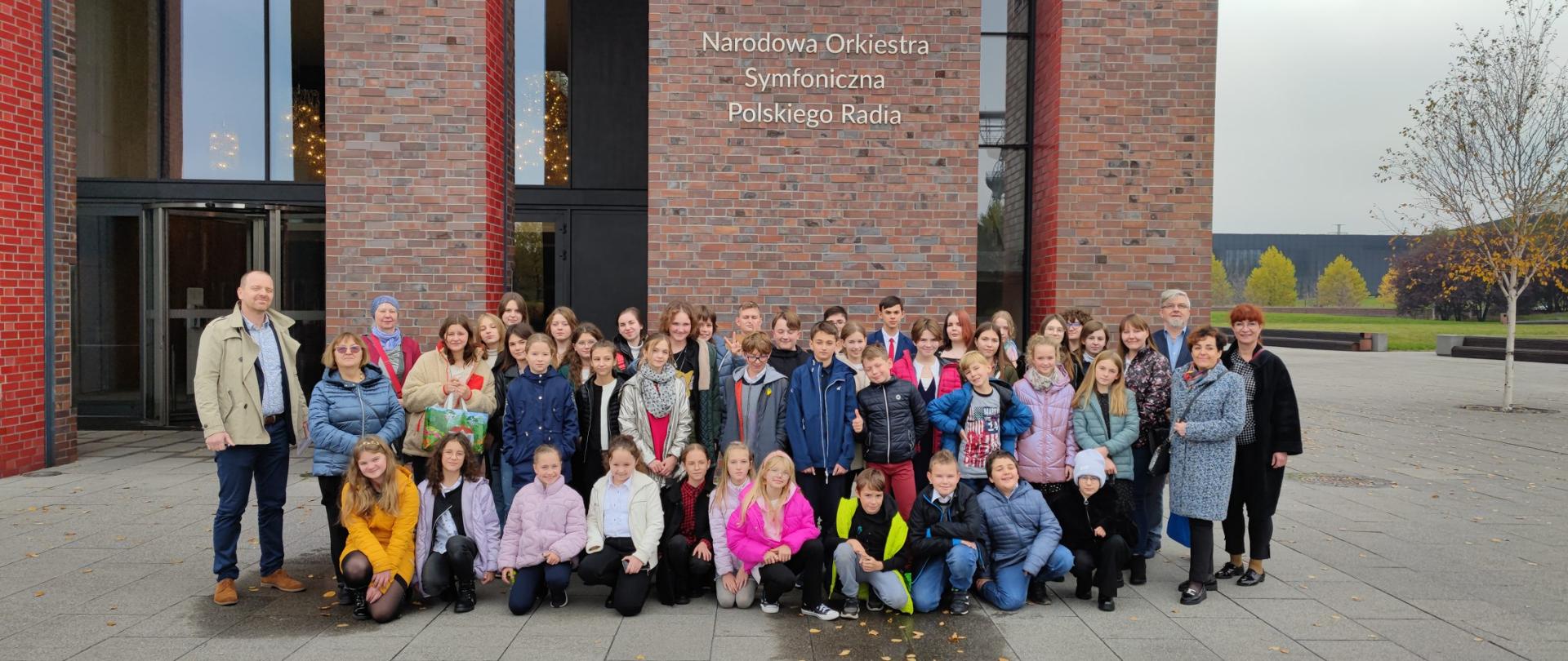 Na zdjęciu znajduje się grupa uczniów wraz z pedagogami PSM I st. w Jaśle na tle wejścia do budynku Narodowej Orkiestry Polskiego Radia w Katowicach