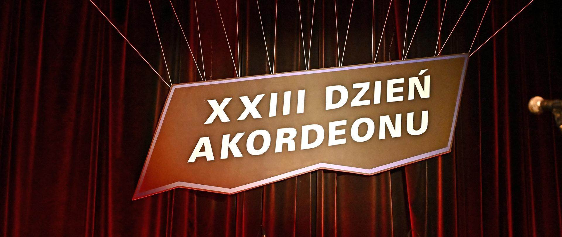 Kolorowy baner wywieszony na scenie sali koncertowej Kłodzkiego Ośrodka Kultury z tekstem "XXIII Dzień Akordeonu"