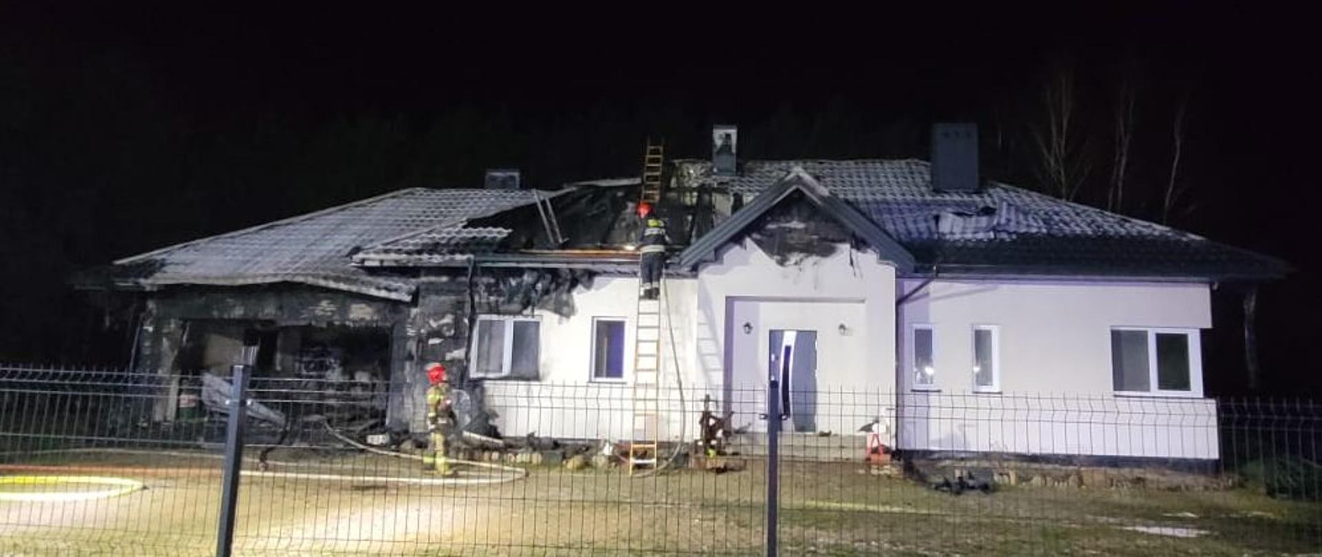 dom jednorodzinny po ugaszonym pożarze, strażacy przy budynku na drabinie. jedna część domu spalona