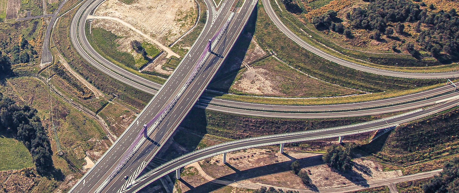 Zdjęcie lotnicze autostrady A1 w Mszanie. Na zdjęciu widoczny wiadukt w ciągu autostrady, pod którym przechodzi drogowa łącznica węzła w Mszanie. W górnej części fotografii widoczny wiadukt, którego konstrukcję nośną stanowią dźwigary łukowe, w ciągu drogi wojewódzkiej 933.
