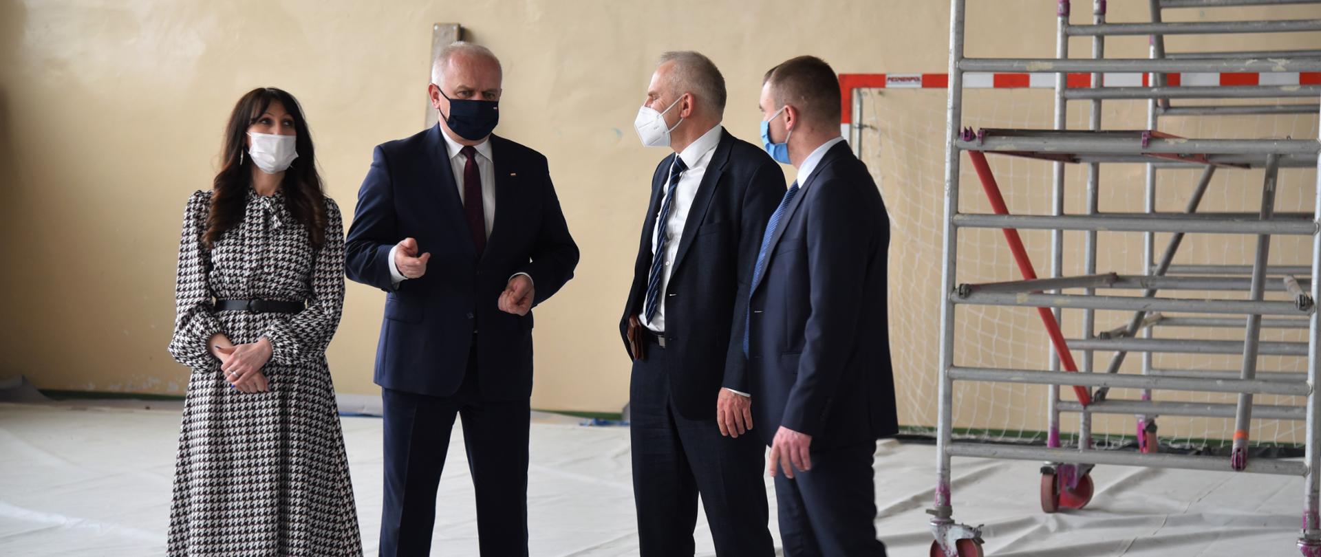 Wojewoda, dyrektorka szkoły, starosta i radny rozmawiają w remontowanej sali gimnastycznej. 