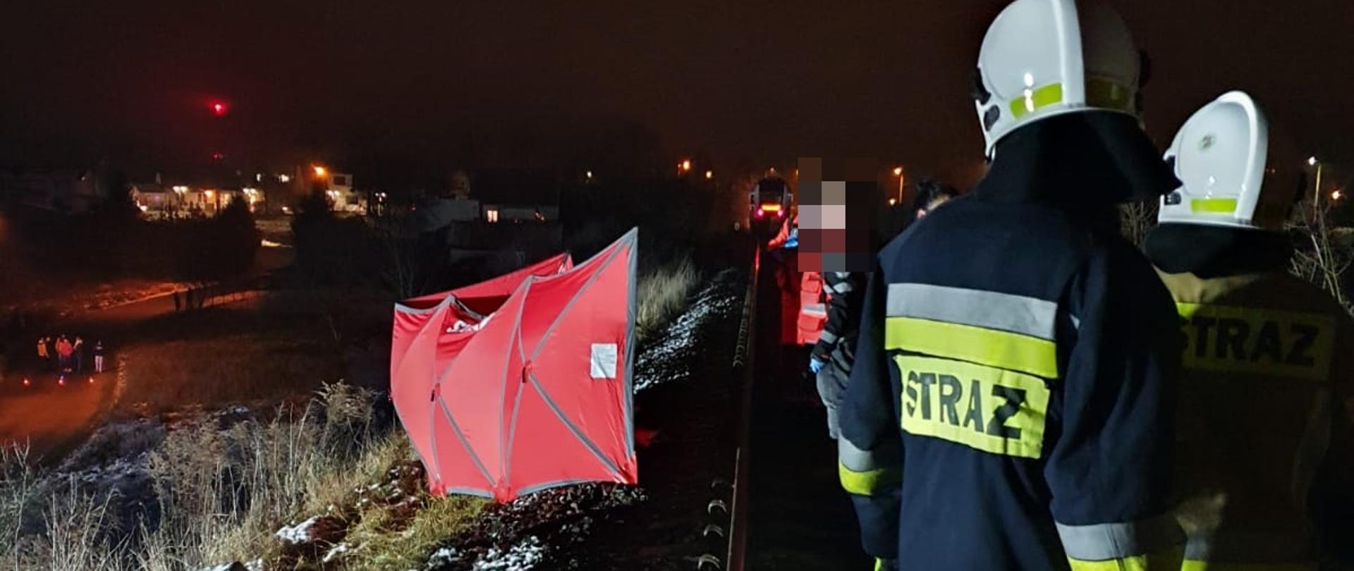 Na zdjęciu widać miejsce zdarzenia odgrodzone parawanem oraz strażaków