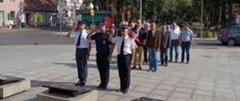 Rocznica wybuchu Powstania Warszawskiego. Plac przed pomnikiem Żołnierza Polskiego w Rawiczu. Delegacja PSP, SW i Policji składa wiązankę kwiatów na płycie pomnika. Funkcjonariusze salutują.