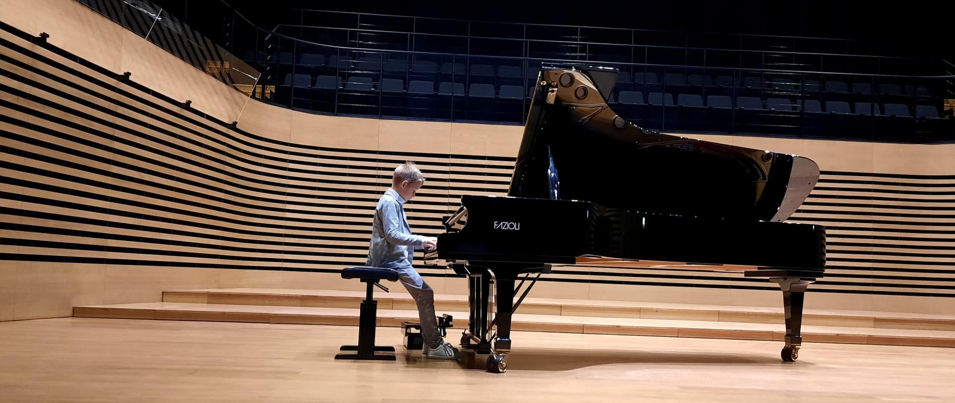 Chłopiec gra na fortepianie Fazioli na estradzie sali koncertowej.