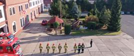 Zdjęcie z drona (z góry) przedstawia strażaków podczas uroczystego podnoszenia flagi ma maszt