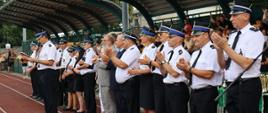 przedstawiciele władz lokalnych łowicza oraz komendanci powiatowi psp w łowiczu wraz z prezesami i druhami ochotniczych straży pożarnych podczas ogłaszania wyników XII powiatowych zawodów sportowo-pożarniczych Ochotniczych Straży Pożarnych z terenu powiatu łowickiego, w tle trybuny z kibicami