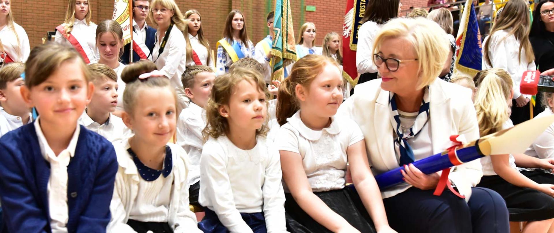 Wiceminister Machałek siedzi obok uczennic Zespołu Szkół z tyłu uczniowie ze sztandarem