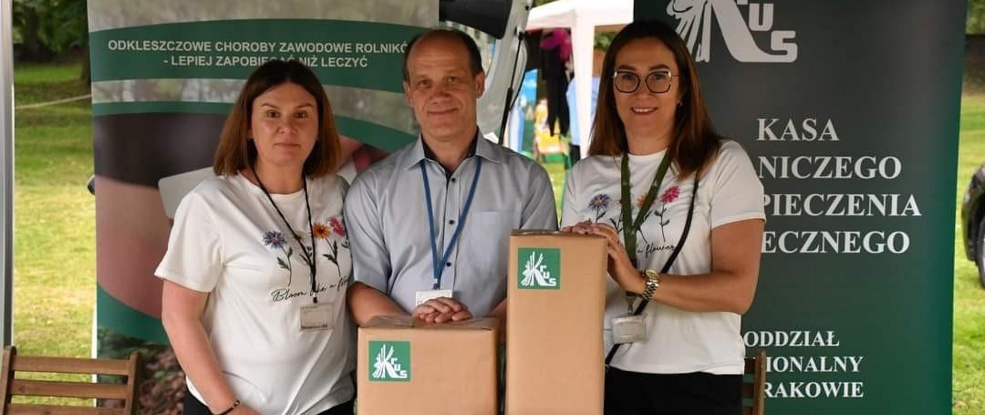Dwie kobiety i mężczyzna przy stoisku z logo KRUS