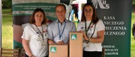Dwie kobiety i mężczyzna przy stoisku z logo KRUS