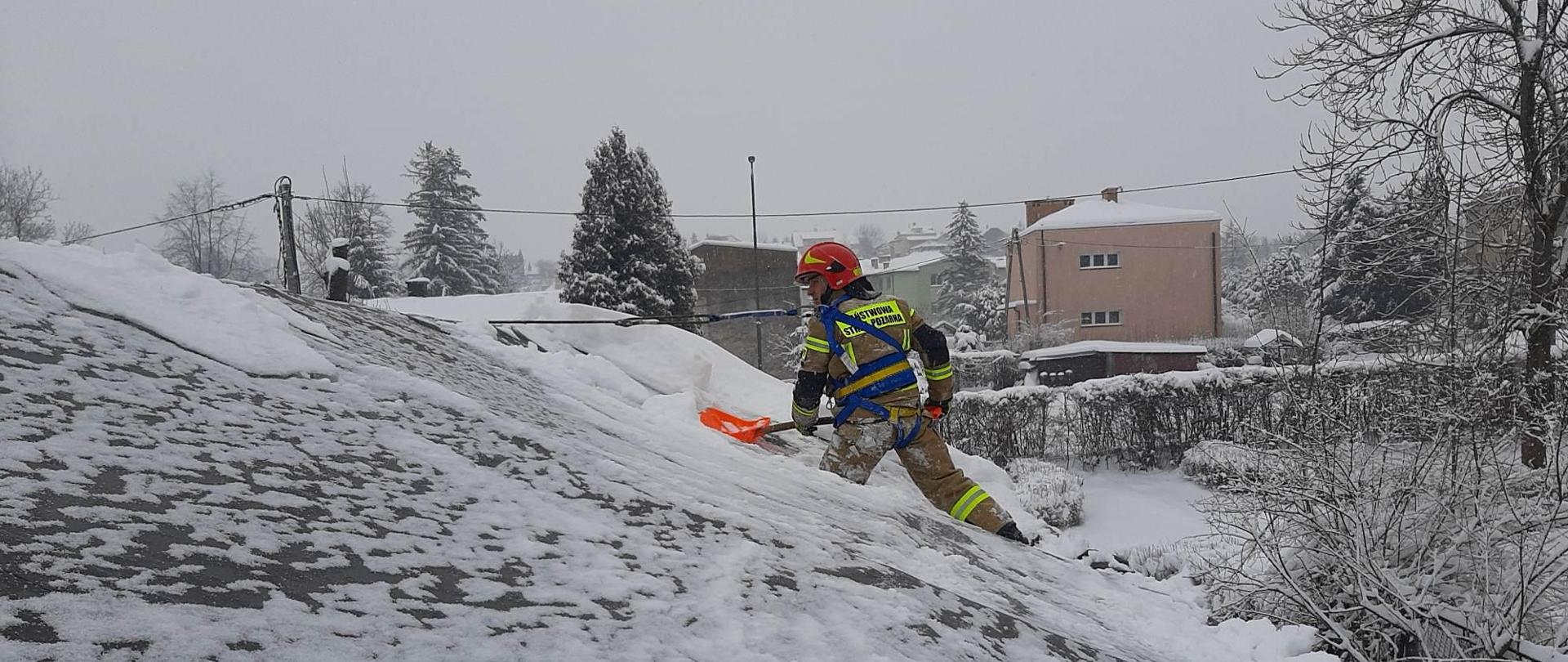 Zdjecie przedtawia ośnieżony dach namiotu. Na dachu znajduje się strażak z łopatą.