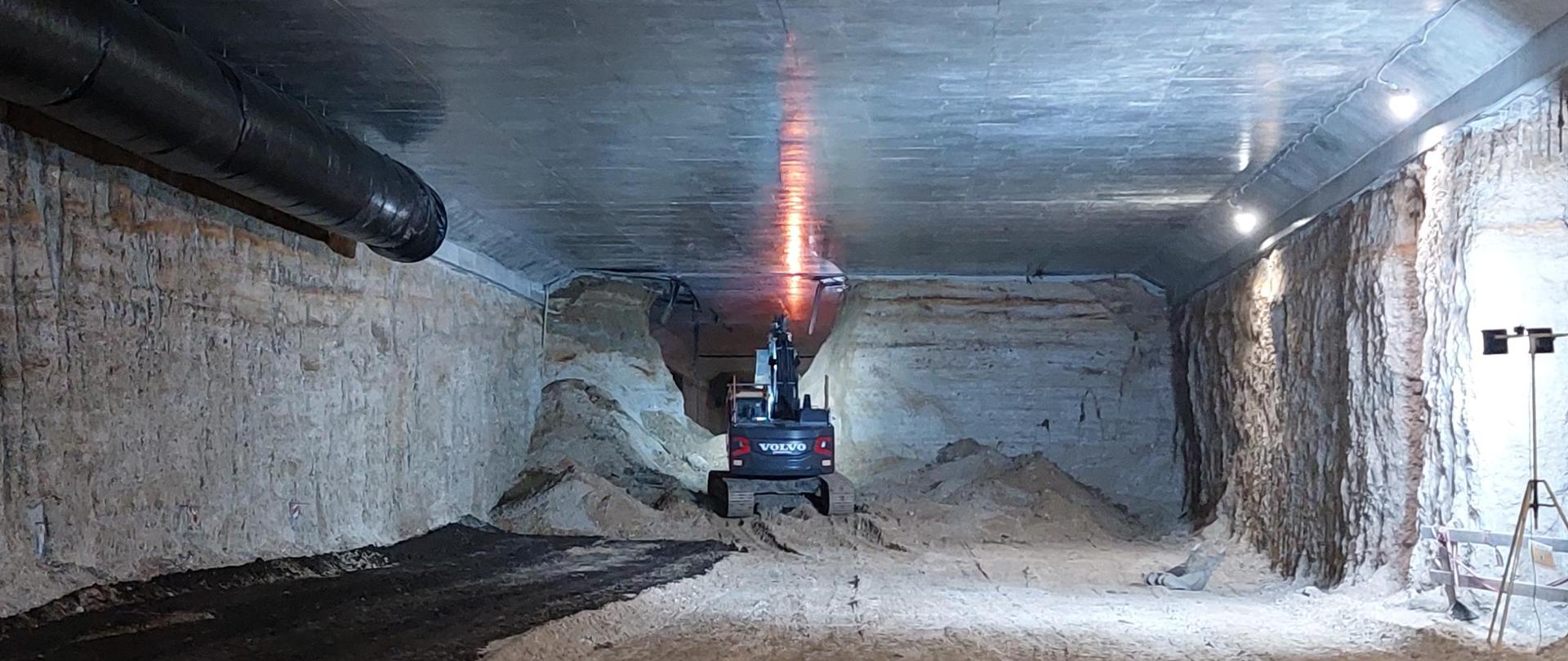 Zdjęcie wykonane we wnętrzu budowanego tunelu na S52, południowej obwodnicy Krakowa. Maszyna budowlana (koparka) usuwa ostatnią warstwę ziemi aby połączyć obie wykopane części tunelu.