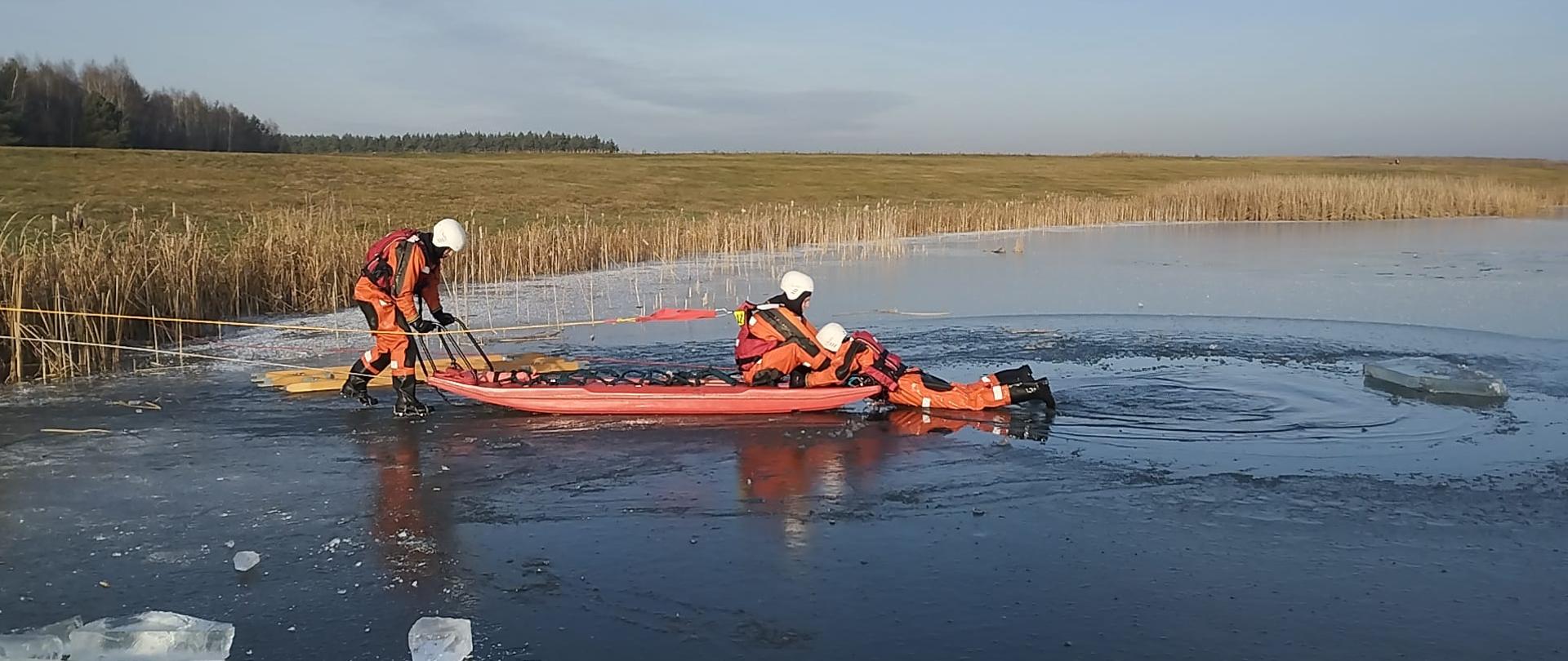 Strażacy w specjalnych stojach ochronnych ratują osobę z zamarzniętego jeziora.