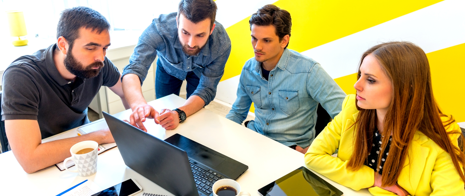 Kobieta i trzech mężczyzn wpatrujących się w monitor laptopa. Jeden z mężczyzn pokazuje pozostałym osobom coś na ekranie.