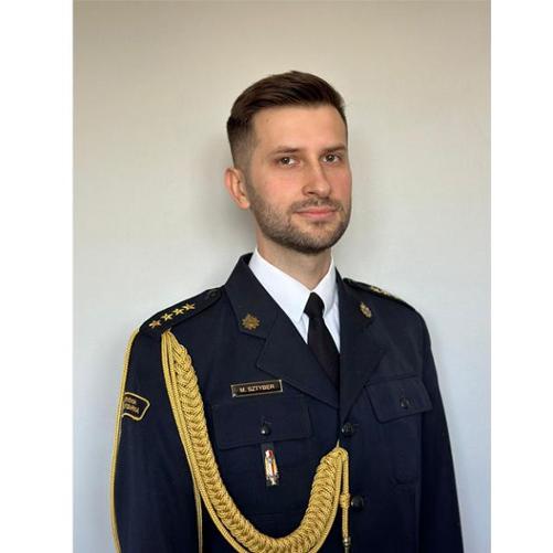 Zdjęcie portretowe p.o. Zastępcy Komendanta Powiatowego Państwowej Straży Pożarnej w Krośnie Odrzańskim (st. kpt. Michał Sztyber) na jasnym tle w mundurze galowym.