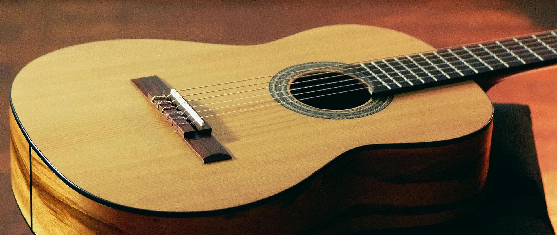 Zdjęcie przedstawia gitarę klasyczną koloru jasnego leżącą na podłodze.