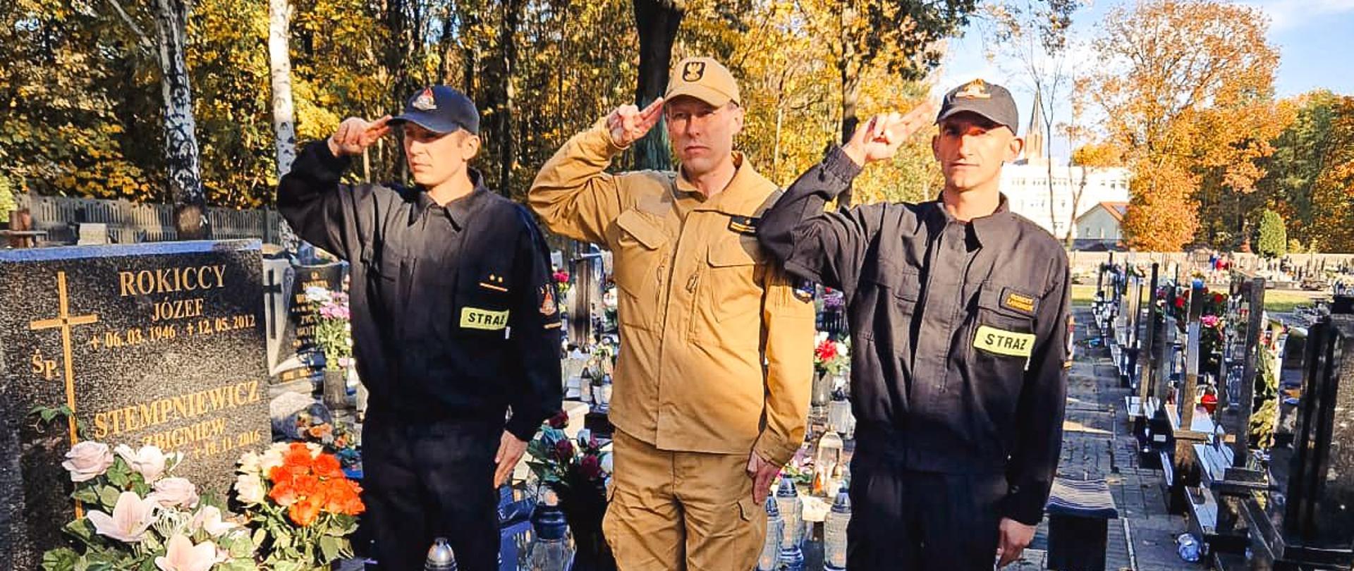 Strażacy oddają hołd przed grobem.