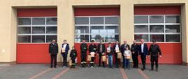 Na zdjęciu widzimy strażaków oraz uczestników eliminacji pozujących z nagrodami na tle Komendy Powiatowej PSP w Pruszczu Gdańskim. 