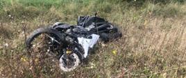 Dzień. Rozbity motocykl leżący na poboczu drogi.