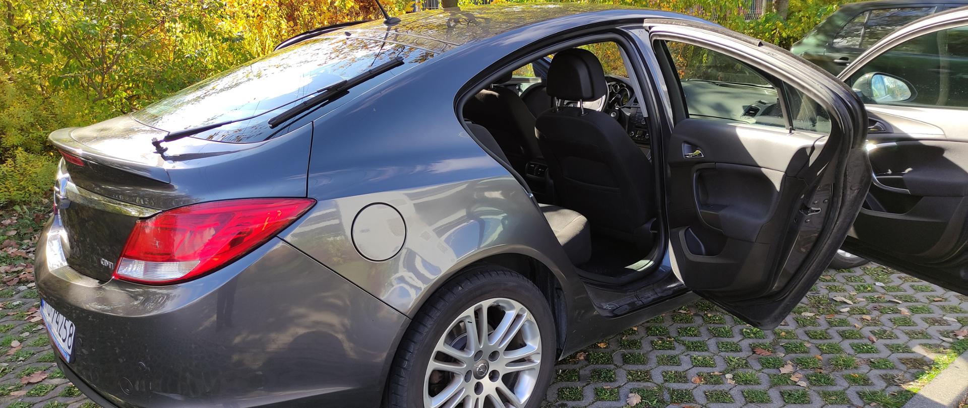 Samochód w kolorze czarnym - Opel Insignia, stoi przed budynkiem i ma otwarte drzwi.