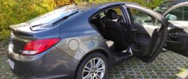 Samochód w kolorze czarnym - Opel Insignia, stoi przed budynkiem i ma otwarte drzwi.